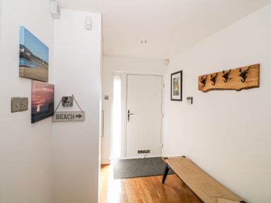 A hallway with a white door a bench wooden floor and wall hooks at Bay View in Trearddur Bay