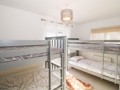 A bedroom with two bunk beds a window with blinds and white curtains at Bay View in Trearddur Bay