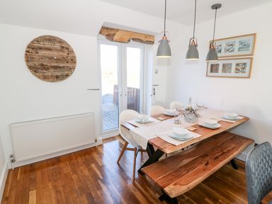 A dining room with wooden table and bench set with dishes and glasses at Bay View in Trearddur Bay