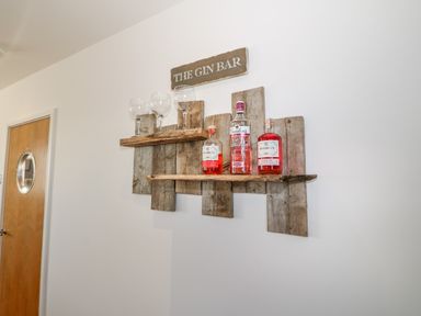 A wall-mounted wooden shelf with gin bottles and glasses under a sign that reads the gin bar