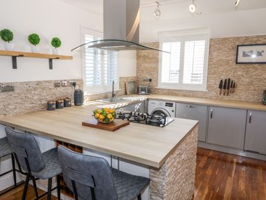 A kitchen with a wooden countertop island and bar stools at Bay View in Trearddur Bay