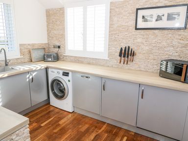 A kitchen with grey cabinets a washing machine a toaster a microwave a knife set and a framed picture at Bay View in Trearddur Bay