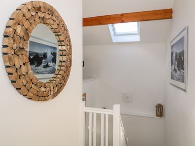 A staircase with white railing a framed photograph on the wall a wooden framed round mirror and a skylight at Bay View in Trearddur Bay
