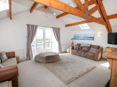 A living room with two sofas a large round ottoman and wooden beams at Bay View in Trearddur Bay