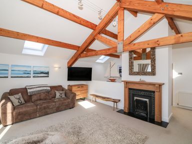 A living room with wooden beams a brown sofa a flat screen tv a wooden fireplace and a decorative sailboat at Bay View in Trearddur Bay