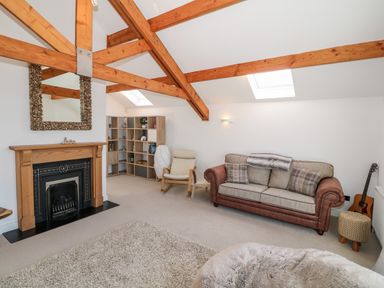 A living room with wooden beams a fireplace a sofa an armchair a bookshelf and a guitar at Bay View in Trearddur Bay