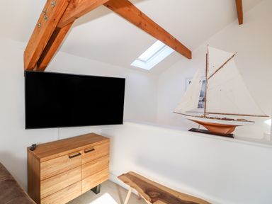 A small room with a wall-mounted TV wooden cabinet wooden bench wooden beams and a model sailboat on a half wall at Bay View in Trearddur Bay