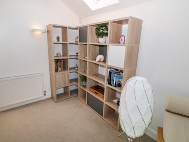 A corner wooden shelving unit with decorative items and books a radiator on the left and a white geometric floor lamp near a cream chair