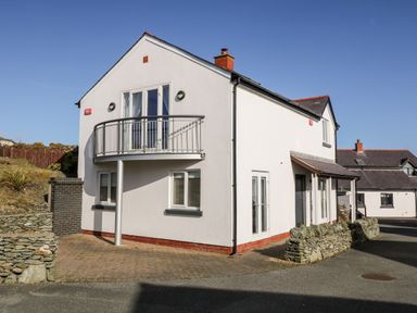 A two story white house with a balcony and stone walls at Bay View in Trearddur Bay