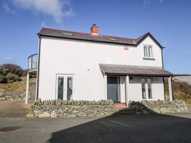 An exterior view of a two-story house with white walls and a stone fence at Bay View in Trearddur Bay