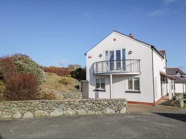 A two-story white house with a small balcony and stone wall outside at Bay View in Trearddur Bay