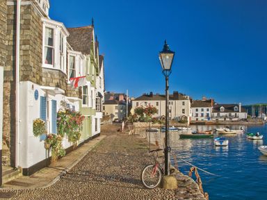 A cobblestone street with houses and hanging flowers next to a harbor with boats at Manor Studio in Dartmouth