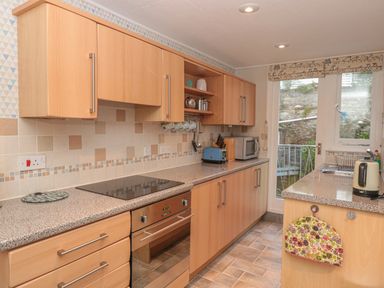 A kitchen with wood cabinets a countertop stove an oven a toaster a microwave a kettle a sink and a door leading outside at Manor Studio in Dartmouth