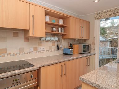 A kitchen with wooden cabinets and beige tiled backsplash a blue toaster a microwave and kitchen utensils at Manor Studio in Dartmouth