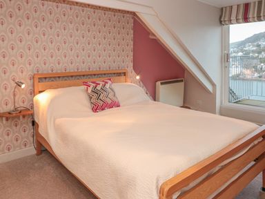A bedroom with a wooden bed with white bedding and a patterned pillow beside a window with a view at Manor Studio in Dartmouth