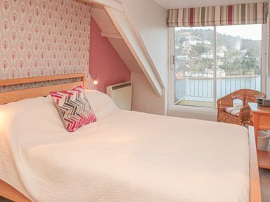 A bedroom with a bed a pillow a wicker chair and a sliding glass door with a view of water and houses at Manor Studio in Dartmouth