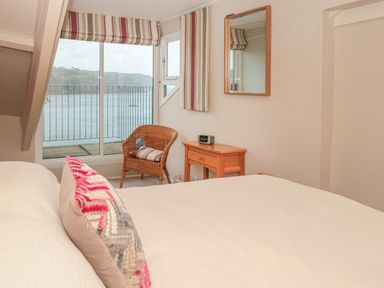 A bedroom with a bed a pillow a wicker chair a wooden table a mirror and a window with a view of water at Manor Studio in Dartmouth