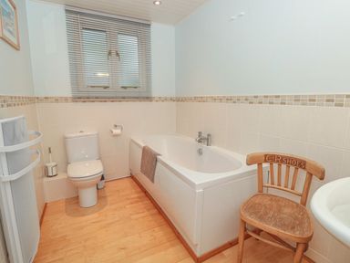 A bathroom with a toilet, bathtub, wooden chair, and window with blinds at Manor Studio in Dartmouth