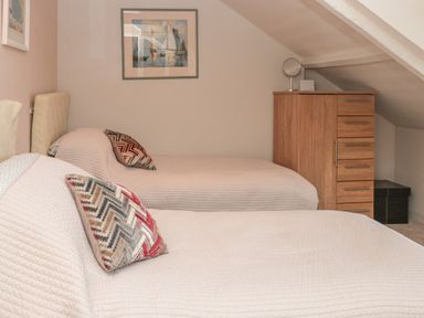 A bedroom with two single beds with patterned pillows a wooden chest of drawers and paintings on the walls at Manor Studio in Dartmouth