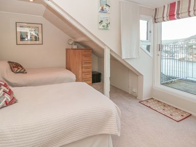 A bedroom with two beds a chest of drawers and a door leading to a balcony overlooking water at Manor Studio in Dartmouth