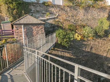 An outdoor area with a metal railing walkway stone walls a small stone building and various plants at Manor Studio in Dartmouth