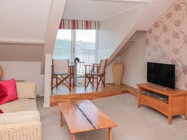 A living room with sofa table chairs tv and sliding glass door overlooking water at Manor Studio in Dartmouth