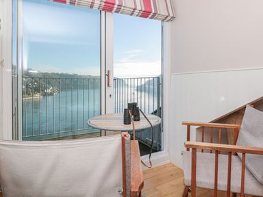 A small seating area with two chairs and a round table with binoculars by a glass door overlooking a river at Manor Studio in Dartmouth