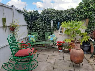 A garden patio with green metal rocking chair and bench with cushions plants and a terracotta chiminea at 21 Florence Road in Pakefield