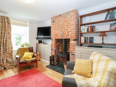 A living room with a brick fireplace wooden shelves with books a gray sofa with yellow cushions and a brown armchair with a yellow throw at 21 Florence Road in Pakefield