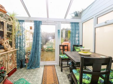 A conservatory with a wooden table and chairs with patterned cushions and an ornate cabinet at 21 Florence Road in Pakefield