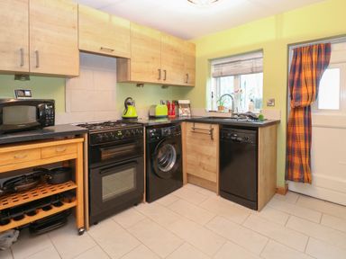 A kitchen with wooden cabinets black appliances and a window with a curtain at 21 Florence Road Pakefield