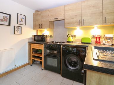 A kitchen with wooden cabinets a black oven a microwave a washing machine and green kettle and toaster at 21 Florence Road in Pakefield