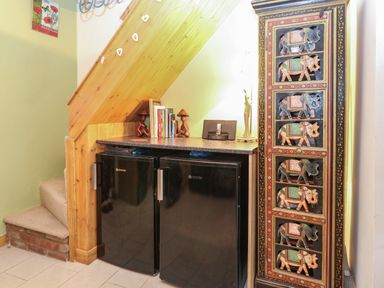 A corner under stairs with two black Hoover mini fridges a countertop with books and lamps and a wooden cabinet with elephant carvings at 21 Florence Road in Pakefield