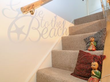 A carpeted staircase with decorative cushions and small figurines on the steps with a handrail on the left and a wall shadow reading Go to the Beach at 21 Florence Road in Pakefield
