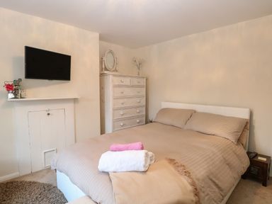A bedroom with a double bed with beige bedding a white chest of drawers a wall mounted television and folded towels on the bed at 21 Florence Road in Pakefield
