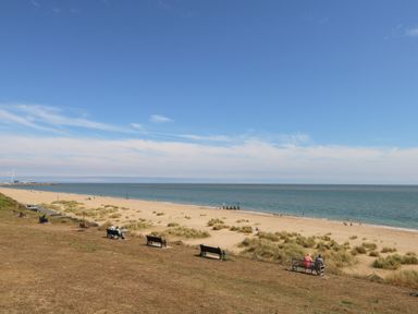 A beach with grass patches benches and people near the sea at 21 Florence Road in Pakefield