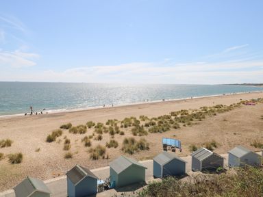 A sandy beach with beach huts along the shore and people walking near the water at 21 Florence Road in Pakefield