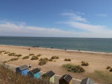 A sandy beach with small beach huts in front and people walking near the water at 21 Florence Road in Pakefield