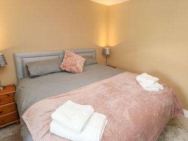 A bedroom with a double bed gray bedding and a pink blanket with folded white towels on it at Crag View in West Woodburn