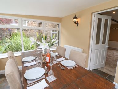 A dining room with a wooden table set with white plates wine glasses and napkins and a vase with white flowers at Crag View in West Woodburn
