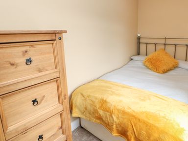 A bedroom with a metal bed frame wooden dresser and a yellow throw at Crag View in West Woodburn
