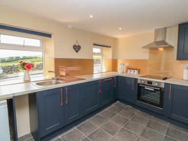 A kitchen with blue cabinets an oven a sink a dish rack and windows overlooking a stone wall at Crag View in West Woodburn
