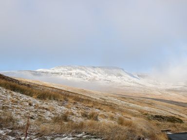 A snow-dusted hillside with a road in the foreground and a mountain with light snow in the background