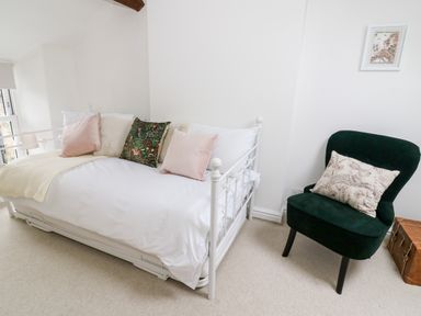A bedroom with a white metal bed with pillows and a dark green chair with a patterned cushion at Pine Cottage in Sedbergh