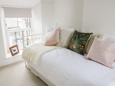 A white daybed with pillows and a knitted throw next to a window with a dog picture on the windowsill at Pine Cottage in Sedbergh