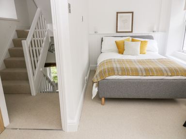 A bedroom with a grey bed with pillows and a yellow blanket next to a stairway in a white room