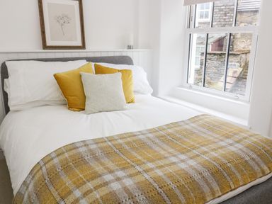 A bedroom with a made bed with white sheets yellow pillows a yellow plaid blanket and a window with a view at Pine Cottage in Sedbergh
