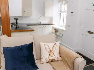 A kitchen area with white cabinets, a sink, a kettle, and a toaster next to a beige sofa with cushions at Pine Cottage in Sedbergh