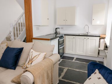 A kitchen with white cabinets a stove and a beige sofa with cushions at Pine Cottage in Sedbergh