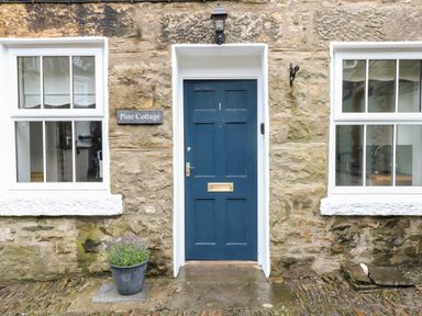 A stone exterior wall with a blue door numbered 1 a plant pot and two windows at Pine Cottage in Sedbergh
